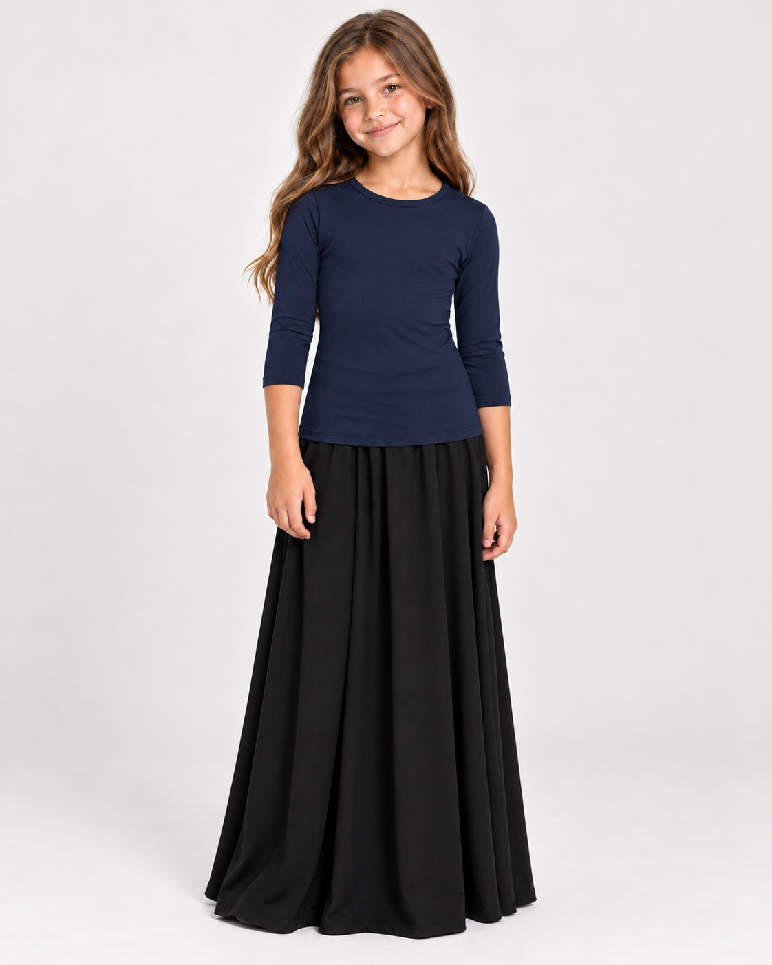 A young girl modeling a navy blue long-sleeve top and a long black skirt against a plain light gray studio background.