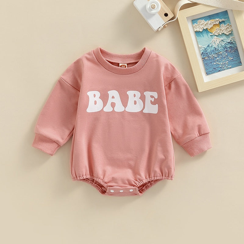 Baby boy or girl wearing a green long-sleeve BABE bubble romper by August + Willow, suitable for 0-3 months, in a cute, cozy setting.