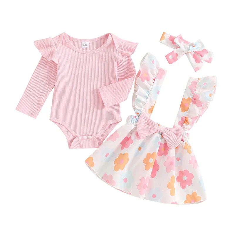 Baby girl fall outfit set with pink long sleeve ribbed romper, bow suspender flower skirt, and matching headband by August + Willow.