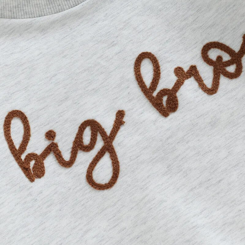 Baby boy in a long sleeve crewneck top with "Big Lil Bro" letters, wearing a matching romper for toddlers, casual and cute.