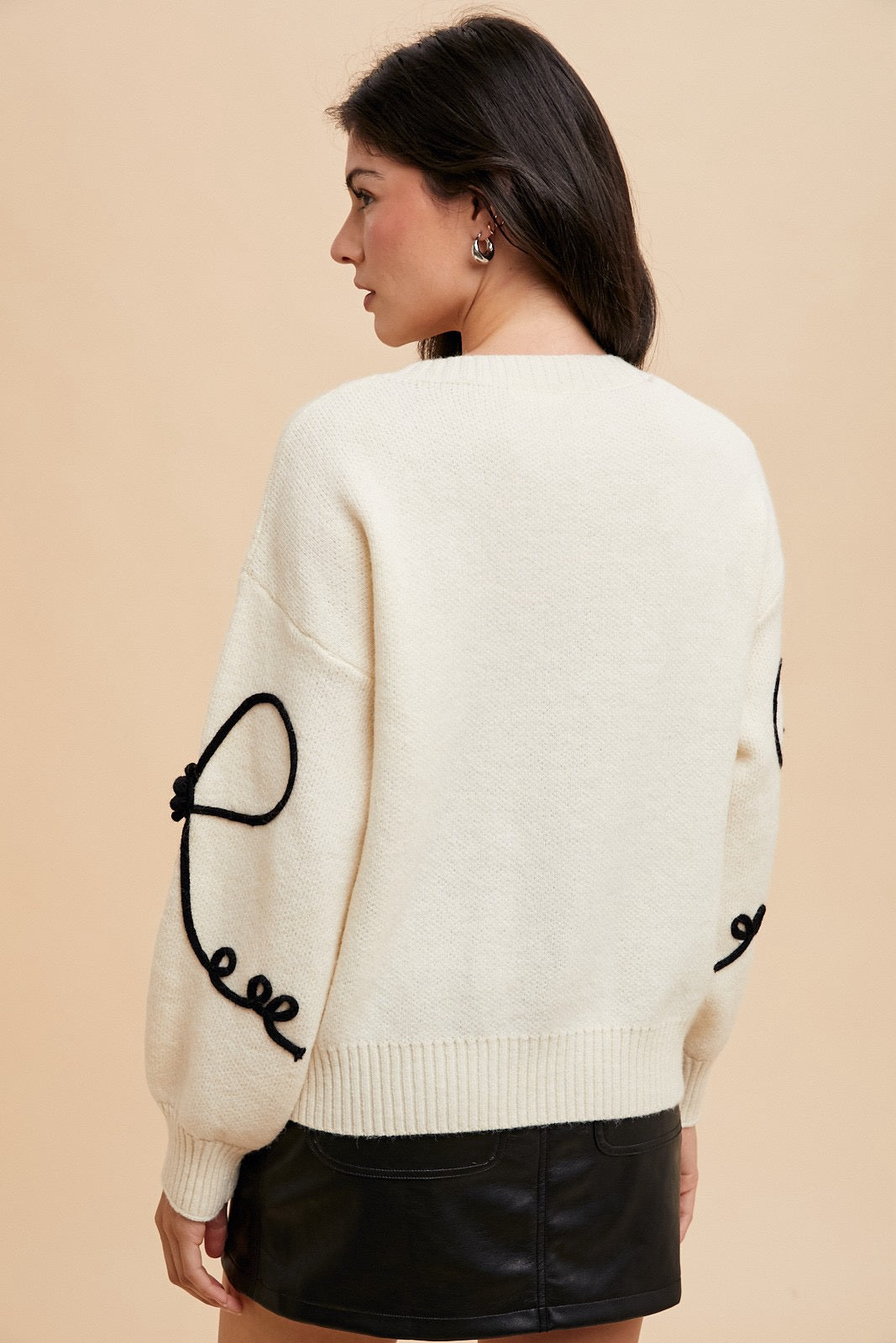 Ivory sweater with black ribbon bow and embroidered trim by Modest and Devoted Designs, showcasing elegant knitwear details.