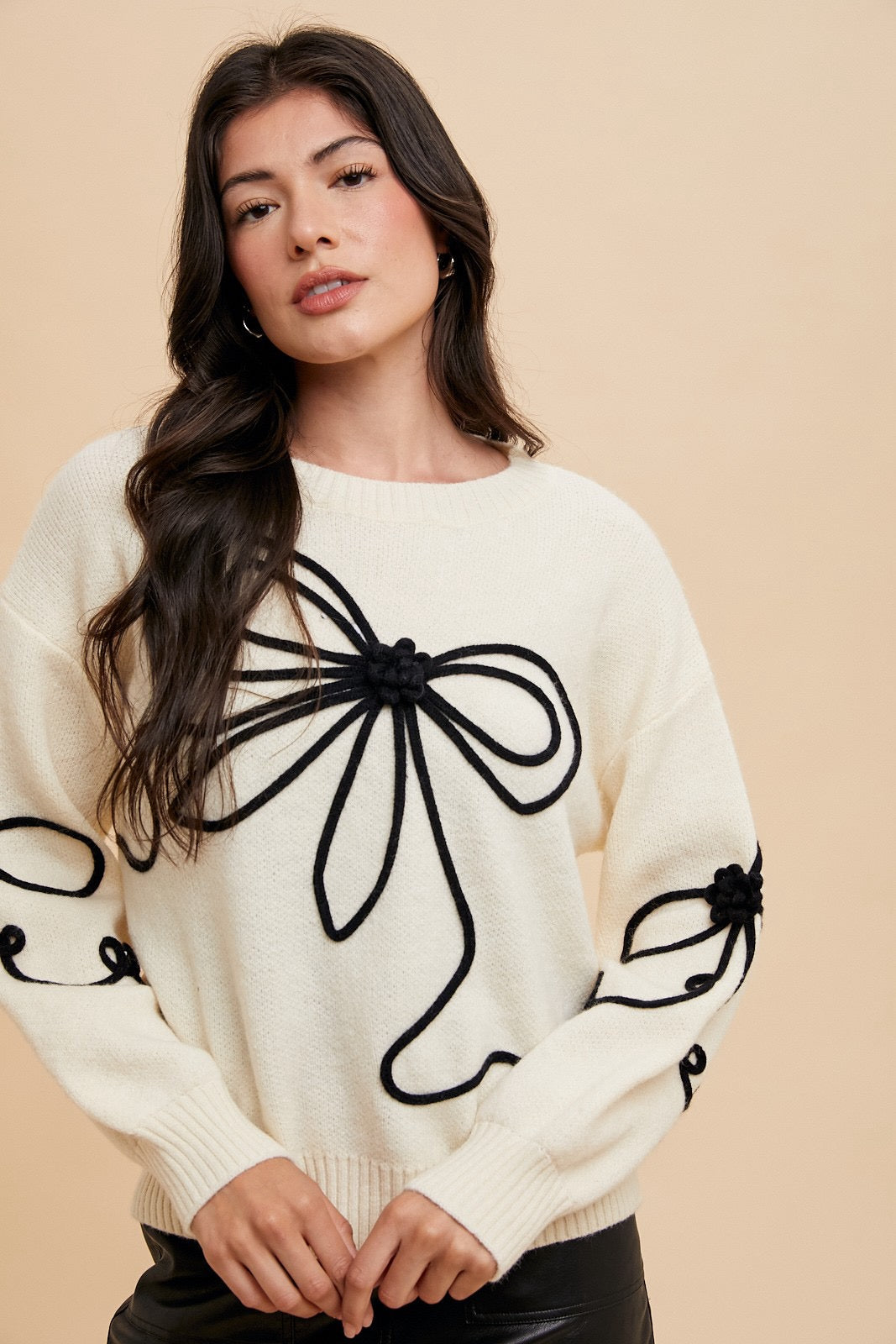 Ivory sweater by Modest and Devoted Designs with black ribbon bow and embroidered trim, showcasing elegant knitwear style.