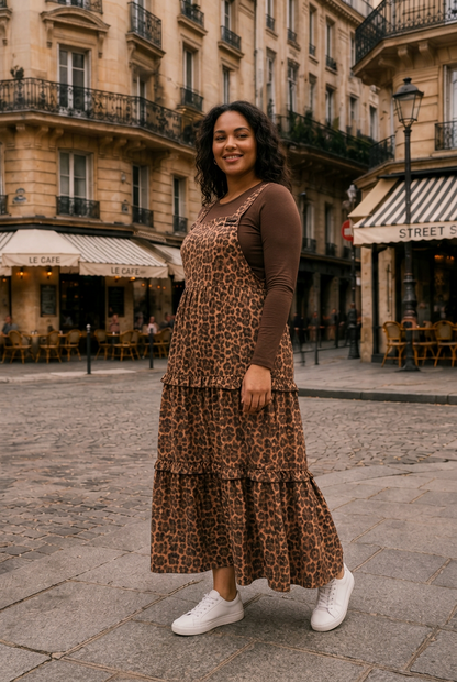 A woman stands on a cobblestone street in front of Parisian-style buildings, wearing a brown and beige leopard-print midi dress over a solid brown long-sleeve top, styled with white sneakers.