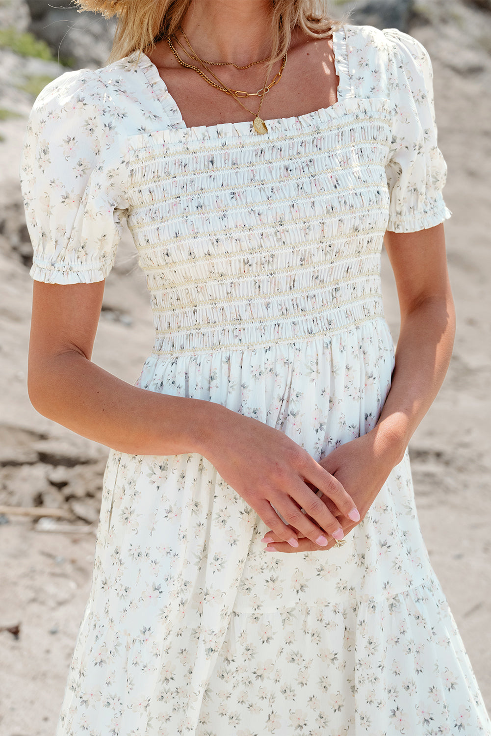 White floral maxi dress with frilly shirred bodice and tiered design by ModestAndDevoted, shown hanging on a white background.