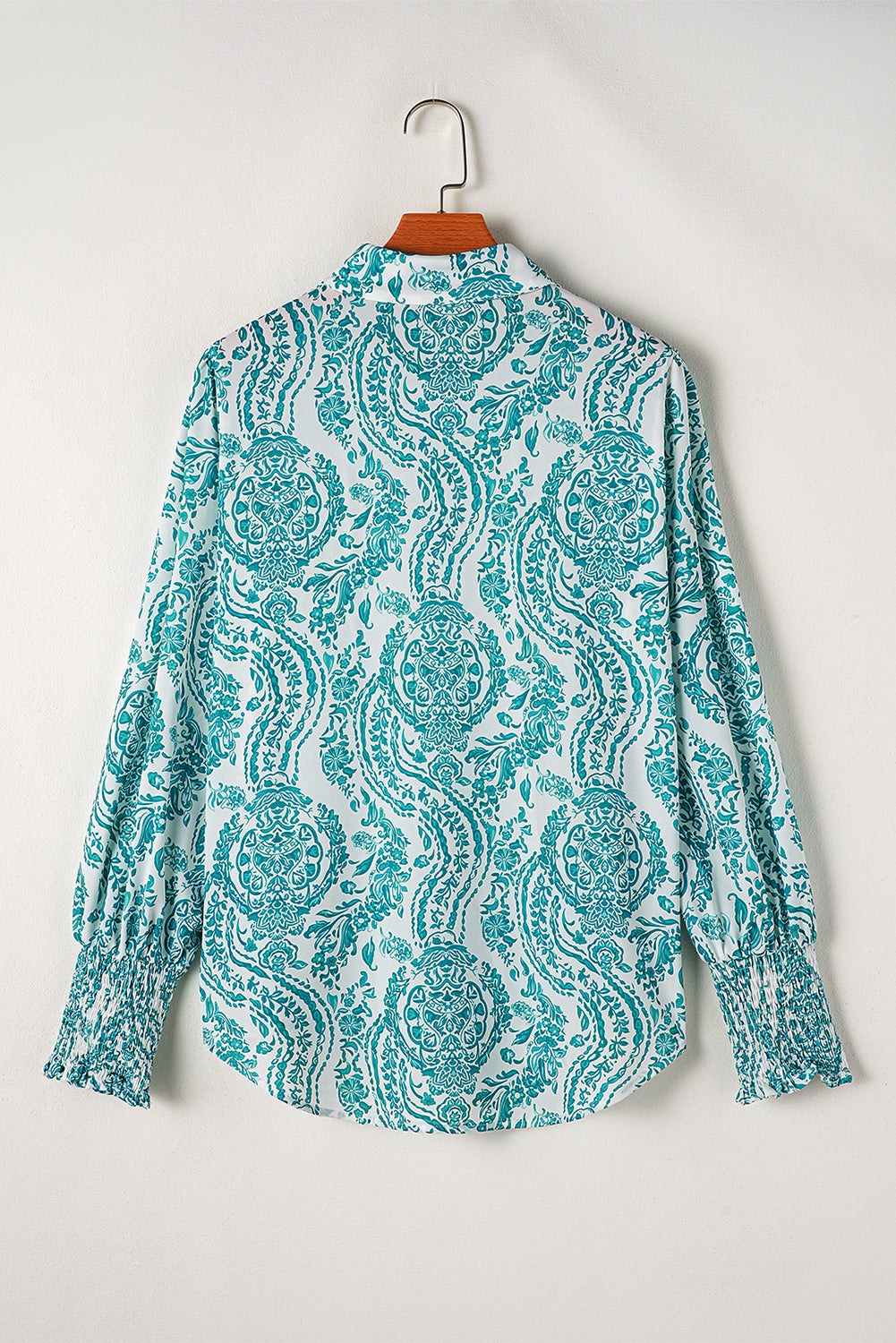 Green paisley print blouse by ModestAndDevoted featuring smocked cuffs, button details, and a loose fit, made of lightweight polyester.